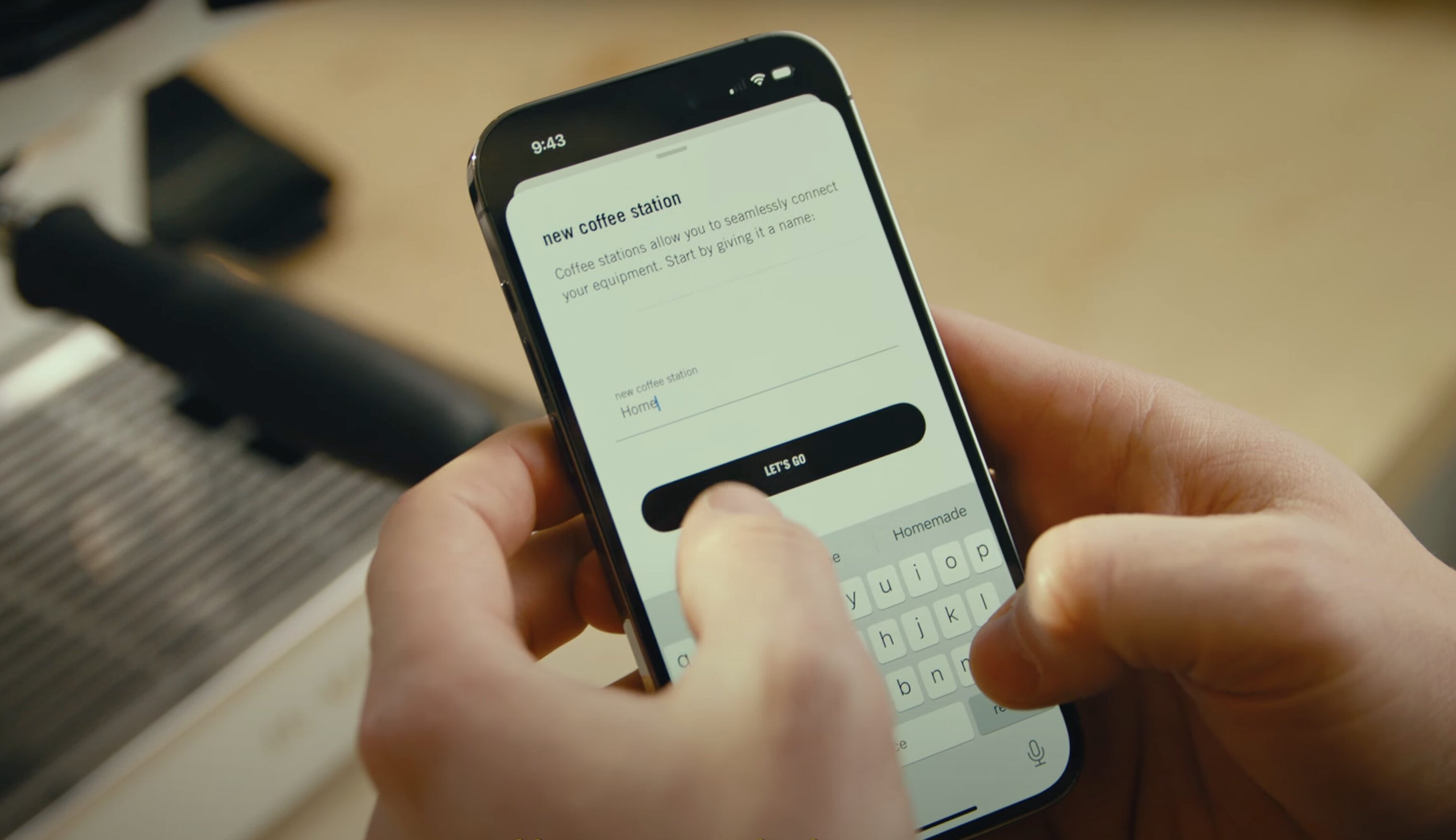 Person using smartphone to enter name for new coffee station setup, with on-screen prompt and keyboard visible